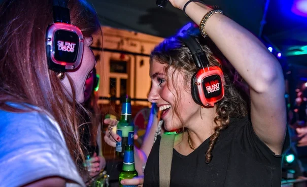 Friends dancing with glowing red LED headphones at silent disco party, sharing drinks and laughter