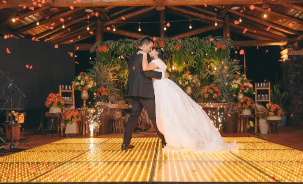 Image showing Bride and groom's first dance on illuminated gold LED dance floor surrounded by rustic floral wedding decor