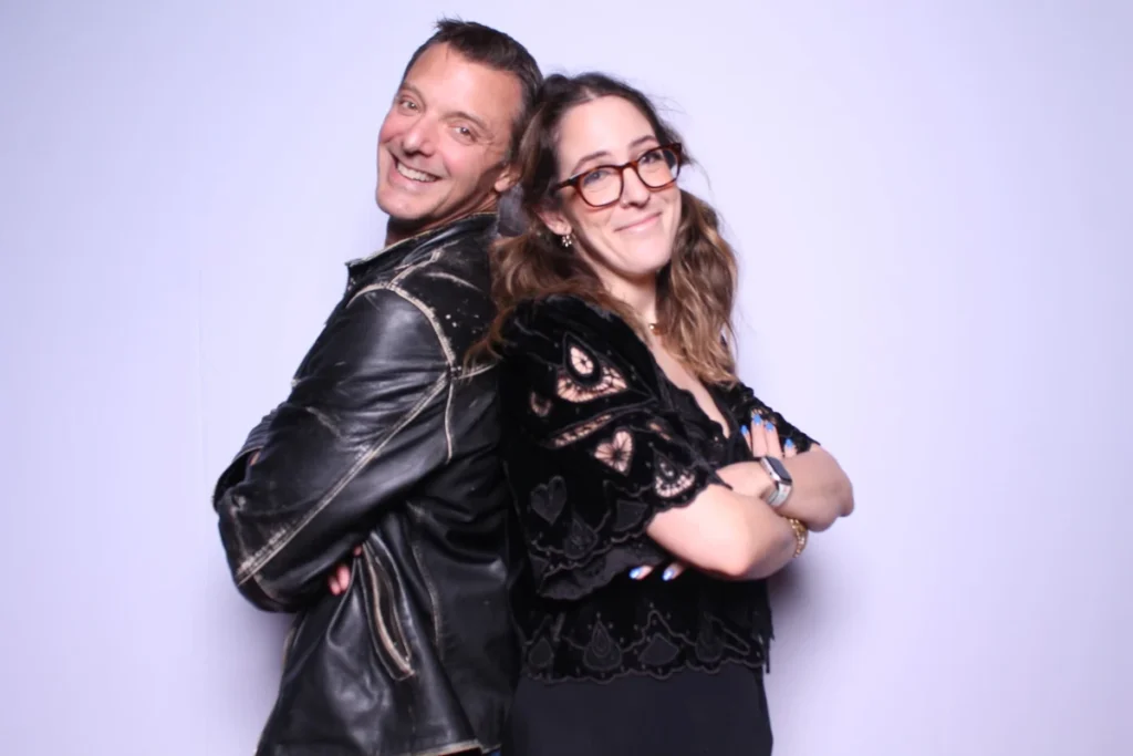 Photo booth back-to-back pose with couple in leather jacket and black dress, casual fun portrait style