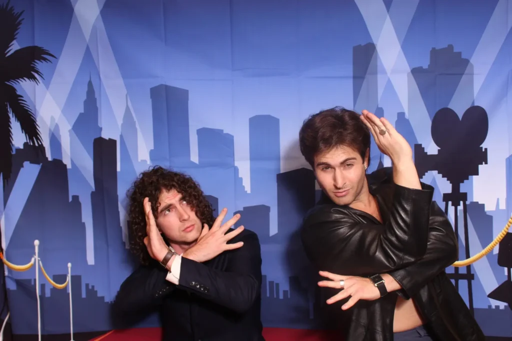 Two people in formal attire posing dramatically in front of an urban skyline backdrop, demonstrating a lively photo booth pose