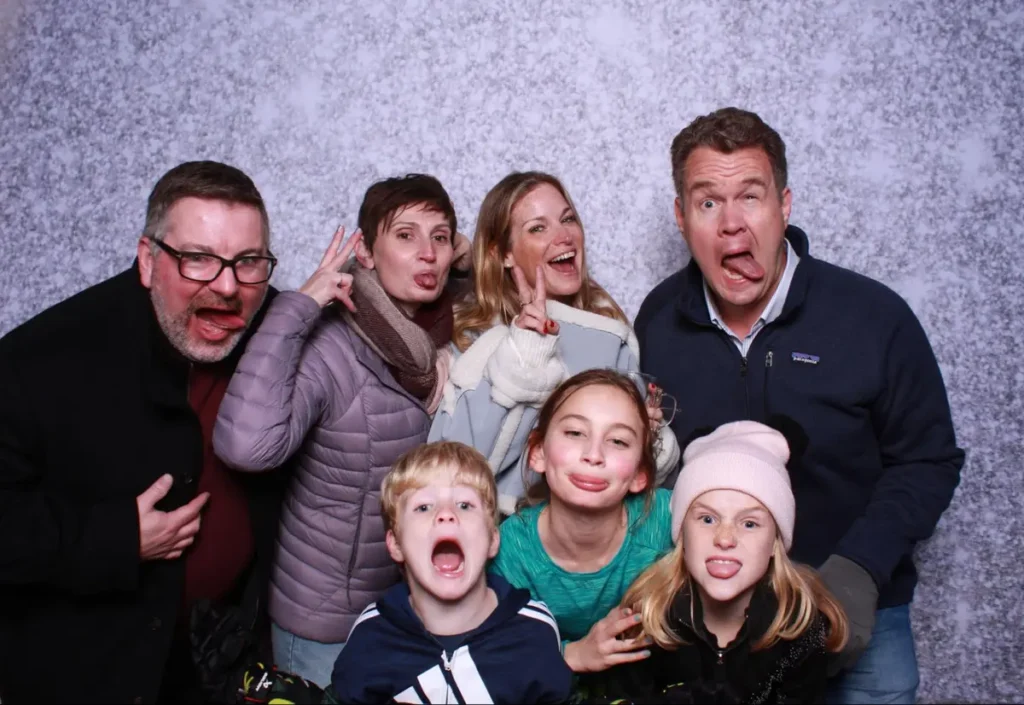 Family photo booth picture with adults and children making silly faces against a textured gray background