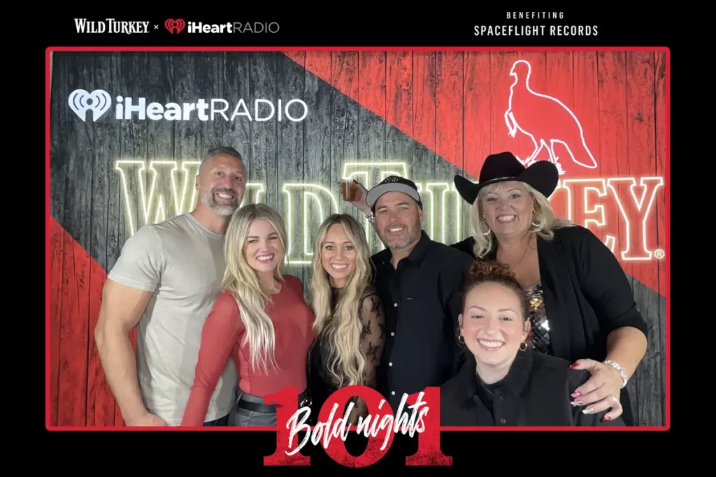 Group photo at Wild Turkey x iHeartRadio branded event booth with rustic wooden backdrop