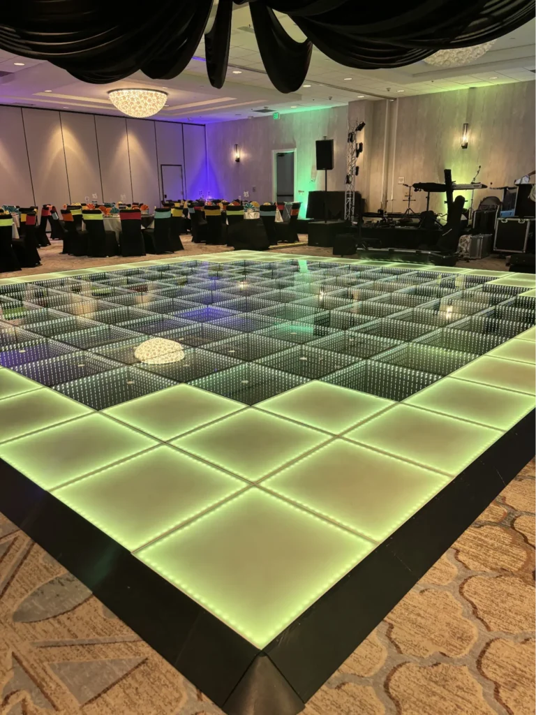 Illuminated LED dance floor with green lighting in a hotel ballroom setup with tables and DJ equipment