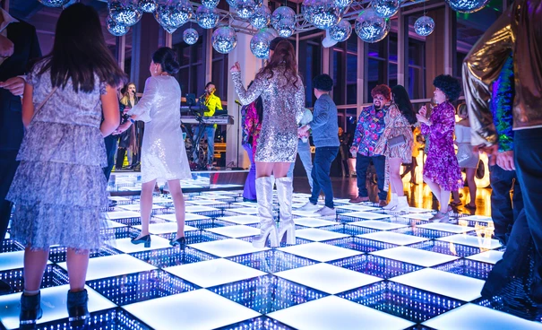 Illuminated LED dance floor with party guests dancing under disco balls at a nightclub event