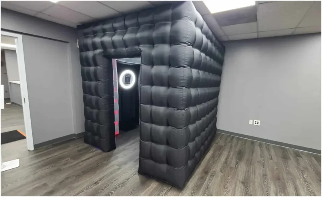 Inflatable black photo booth with LED ring light entrance in office setting, ideal for affordable indoor event rentals