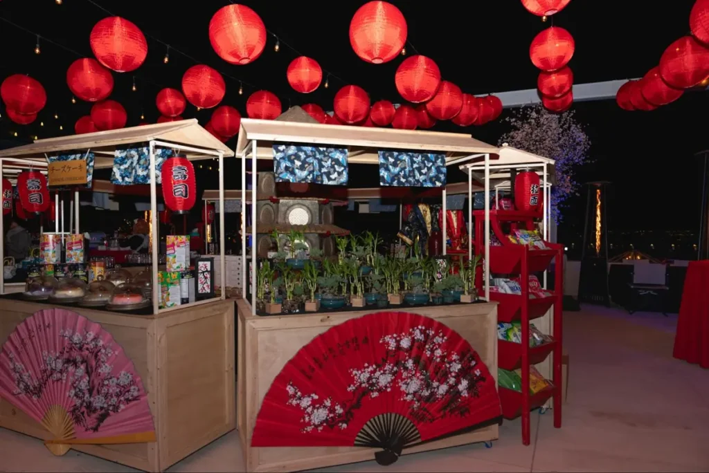 Japanese-themed event setup with red paper lanterns, decorative fans, and small plants in a nighttime setting