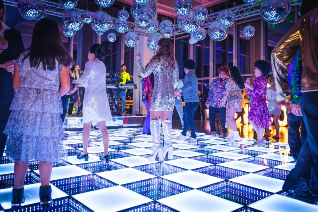 Lively party with illuminated checkerboard dance floor and hanging disco balls creating a vibrant nightclub atmosphere