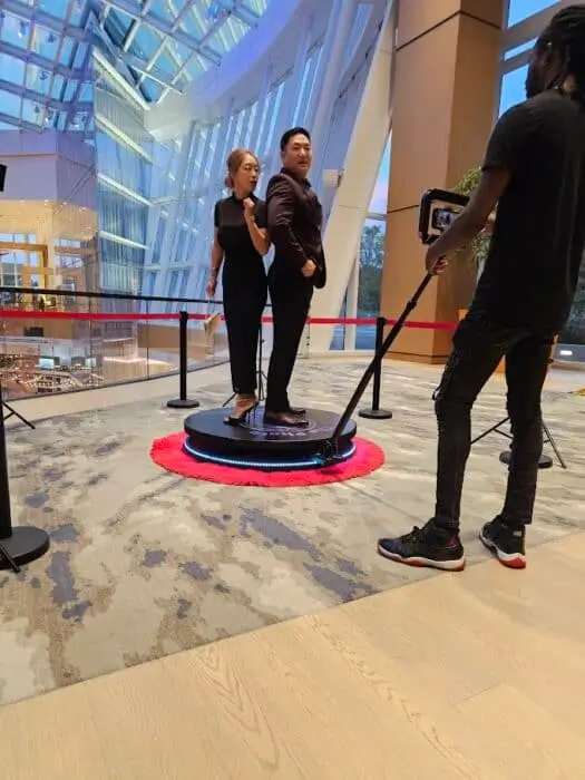 Professional photo shoot setup with two models posing on a circular platform while being photographed in a modern mall atrium