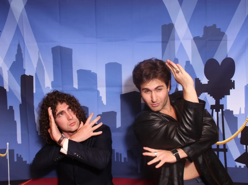 Two young men posing in front of a city skyline backdrop at a photo booth, demonstrating interactive event entertainment options