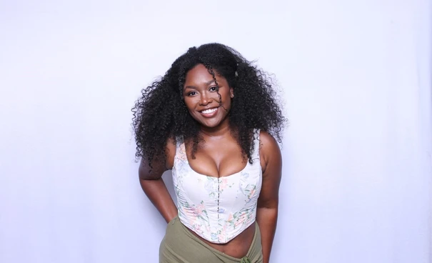 Woman with curly hair smiling in a floral corset top against plain white photo booth background