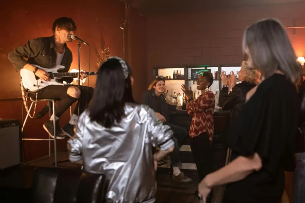 Musician performing on guitar at intimate venue with audience dancing - live music themed event entertainment